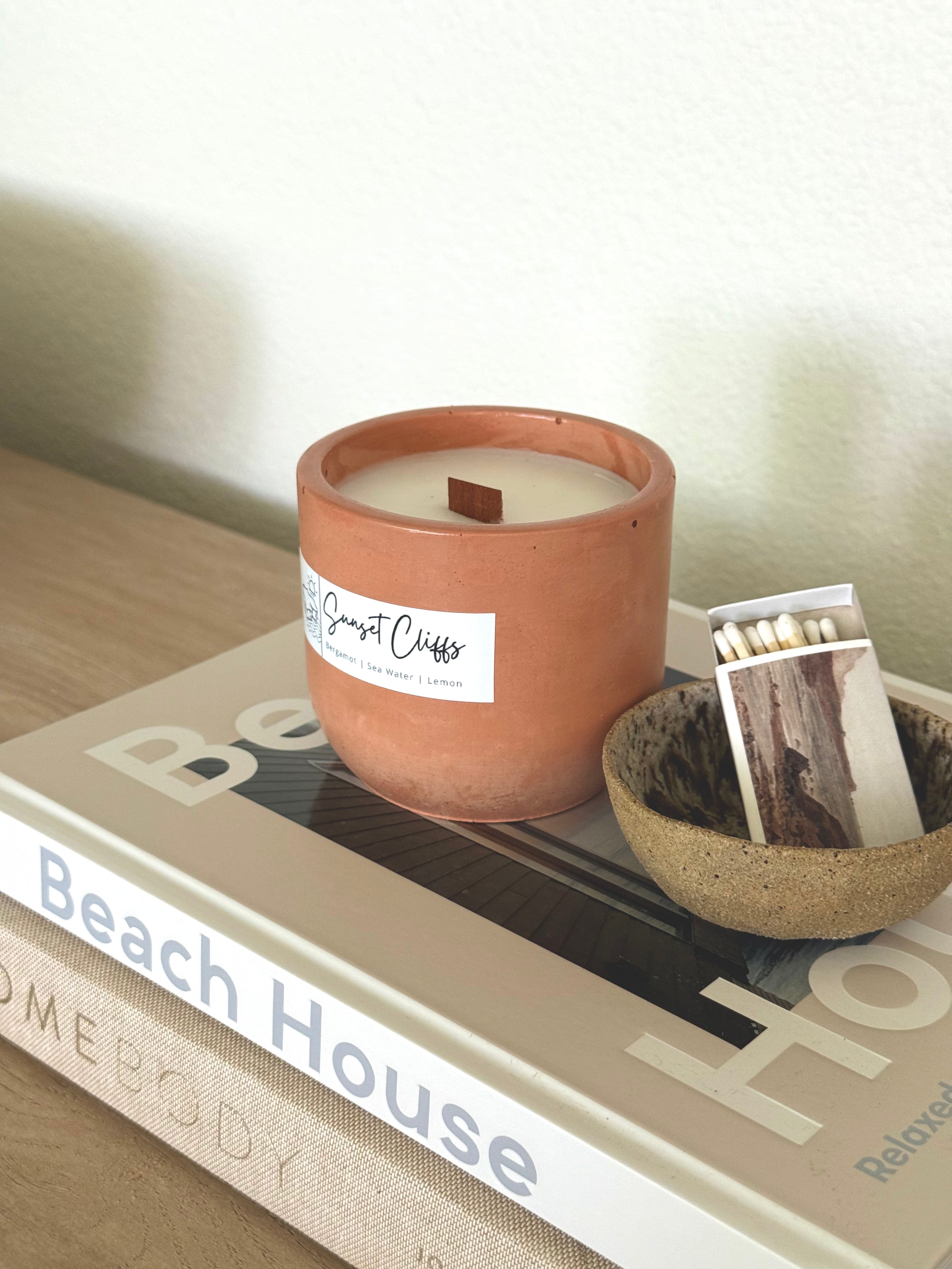 Candle in a terracotta holder with matches on a book titled 'Beach House'.