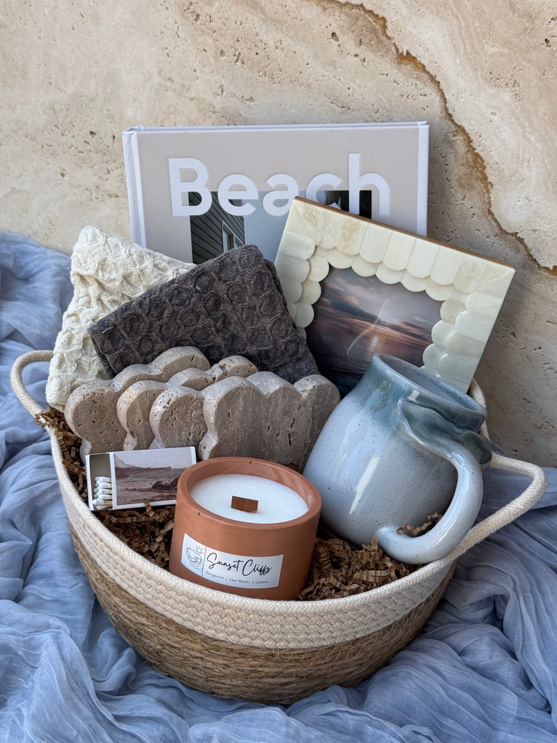Gift basket with a mug, candle, and beach-themed items on a textured surface